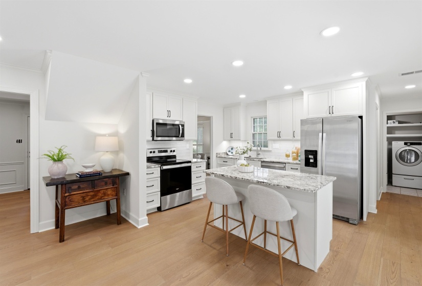 Bright kitchen featuring white cabinetry, stainless steel appliances, a white tile backsplash, and a central island with a light-toned countertop