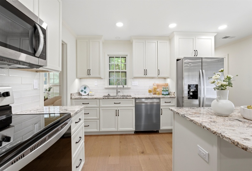 Kitchen with recessed lighting, light wood-finish flooring, white shaker cabinetry, stainless steel appliances, and light-toned patterned countertops
