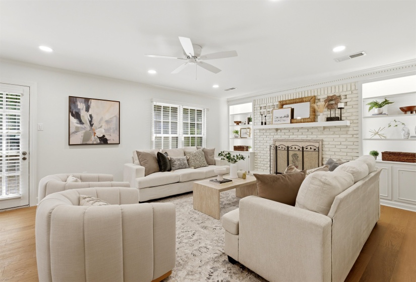Living area featuring a painted brick fireplace with a mantel, built-in shelving, wood-finish flooring, and a ceiling fan