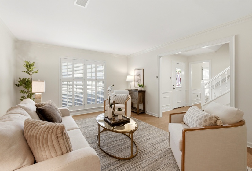 Living area featuring wood-finish flooring, white plantation shutters, crown molding, and a visible entryway with a white paneled door