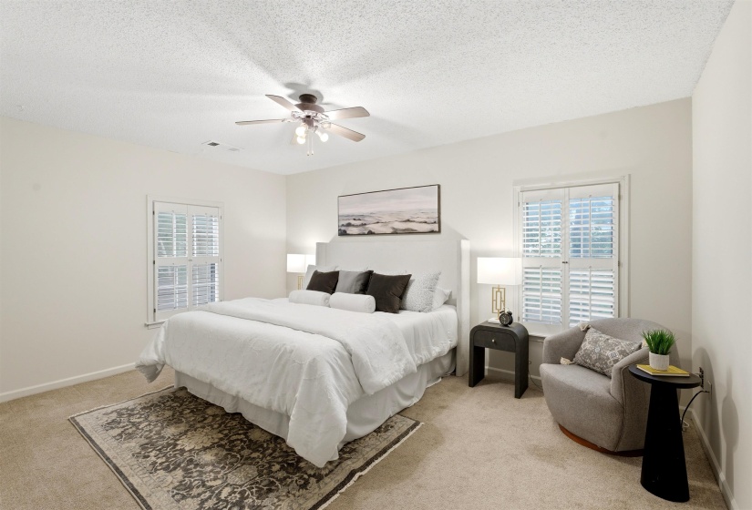 Carpeted room featuring two windows with white plantation shutters, a ceiling fan with integrated lighting, and neutral wall paint