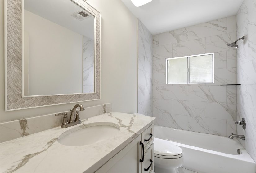 White vanity with a stone-finish countertop, under-mount sink, and brushed nickel faucet