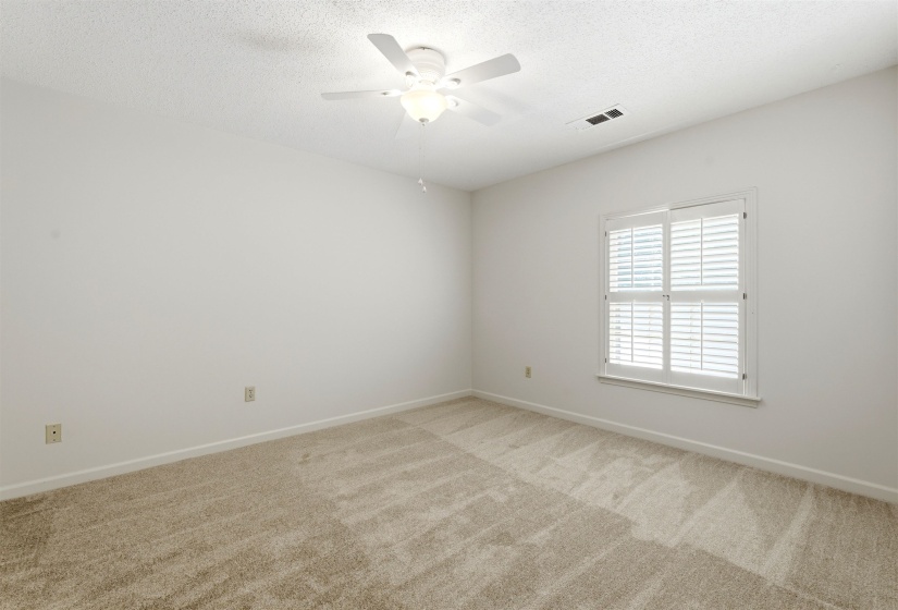 Carpeted room with white walls, a single window featuring white plantation shutters, and a ceiling fan with integrated lighting