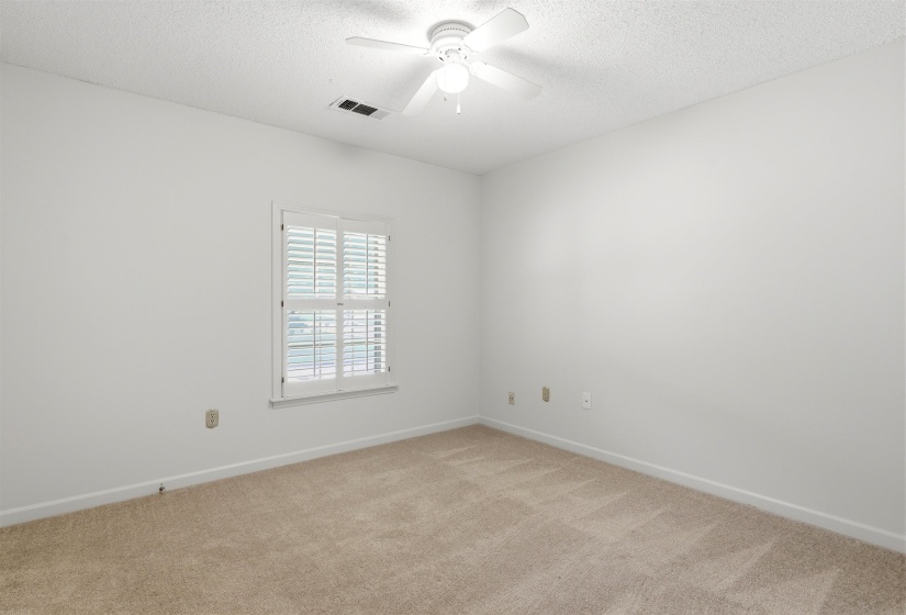 Neutral wall paint complementing textured carpeting, a white window frame with louvered blinds, and a white ceiling fan with integrated lighting