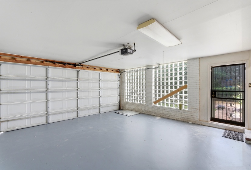 Garage space featuring a painted concrete floor, two white panel garage doors, glass block windows, and a side entry door with an ornamental security screen