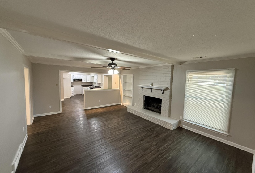 Spacious living area featuring wood-finish flooring, a white-painted brick fireplace with mantle, and a built-in bookshelf