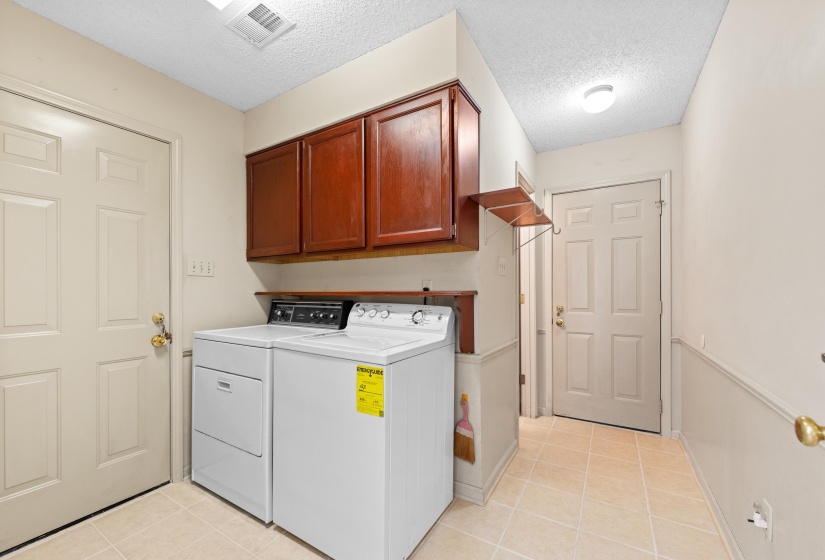 Utility area featuring light-toned tile flooring, wainscoting, and overhead cabinetry