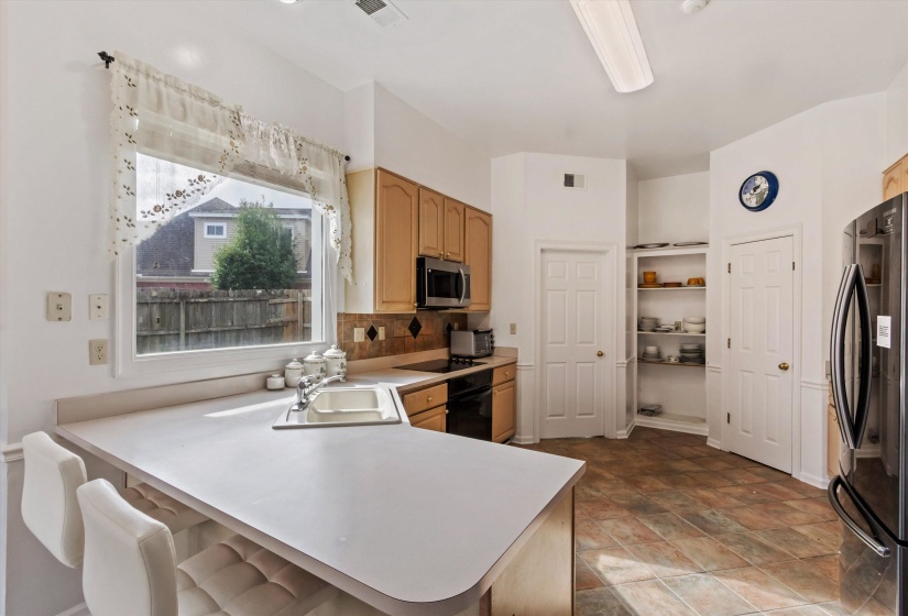 Kitchen with a peninsula, black appliances, light countertops, and a kitchen breakfast bar