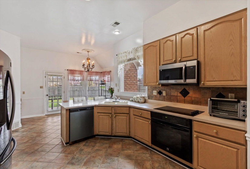 Kitchen featuring a peninsula, tasteful backsplash, light countertops, black appliances, and lofted ceiling