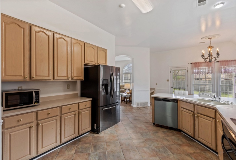 Kitchen with arched walkways, stainless steel appliances, light countertops, suspended lighting, and light wood finish cabinets
