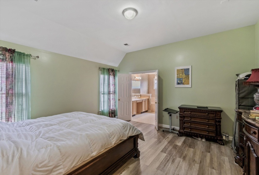 Bedroom with light wood finished floors, lofted ceiling, and ensuite bathroom