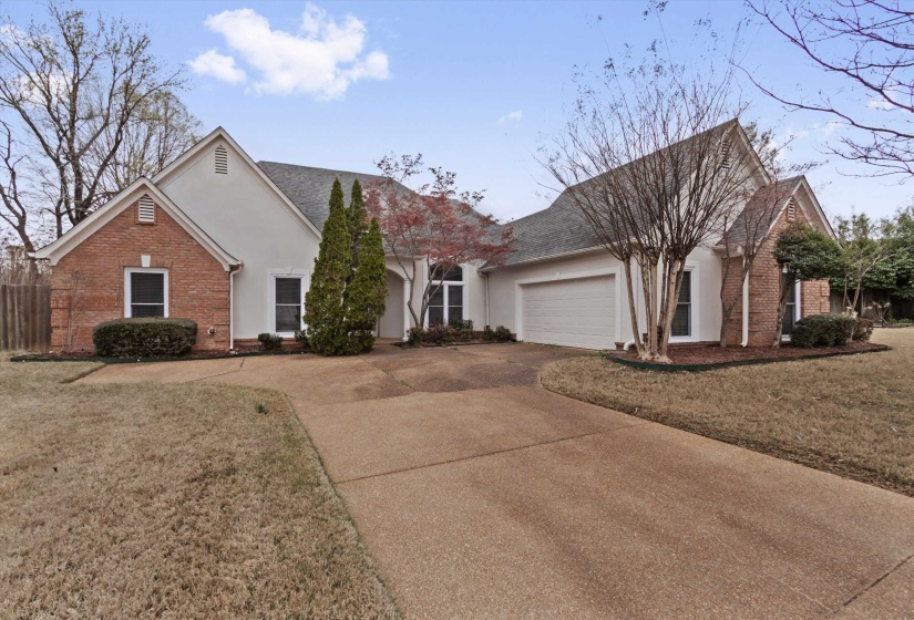 View of front facade with brick siding, a front lawn, driveway, an attached garage, and stucco siding