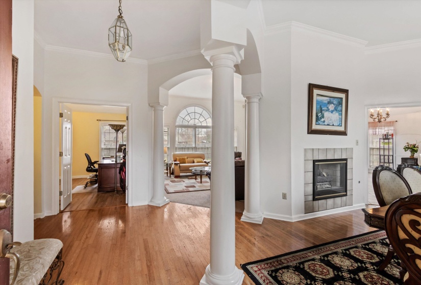Entrance foyer featuring crown molding, ornate columns, light wood-style flooring, a chandelier, and arched walkways