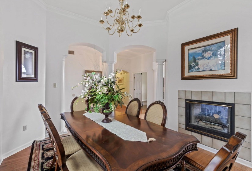 Dining area with arched walkways, wood finished floors, a fireplace, hanging lights, and ornamental molding