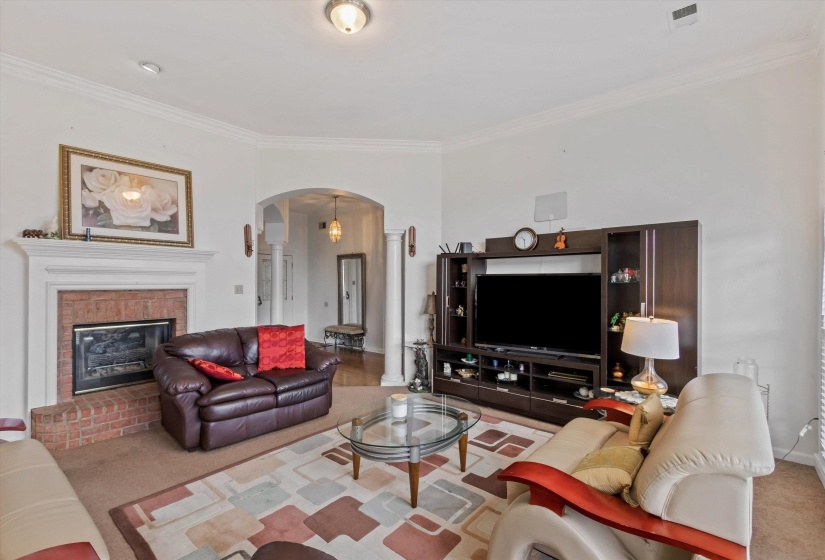 Carpeted living room with arched walkways, crown molding, and a brick fireplace