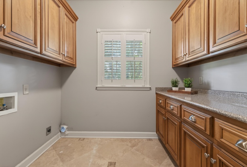 Laundry room featuring extensive wood cabinetry, a window with plantation shutters, a durable countertop, and tile flooring