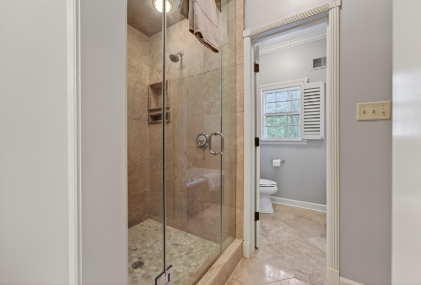 Glass-enclosed shower featuring natural stone-finish wall tile, pebble-tile flooring, and a built-in shower niche