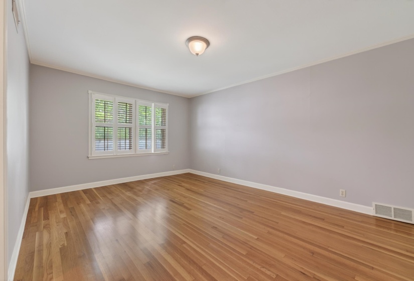 Room featuring wood flooring, neutral tone walls, white trim, a single window with white plantation shutters, and a ceiling-mounted light fixture