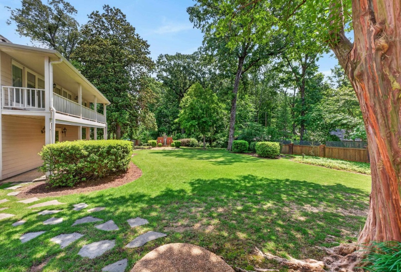Expansive green lawn framed by mature trees, featuring a light-colored exterior with a two-story balcony, decorative railings, and foundation plantings