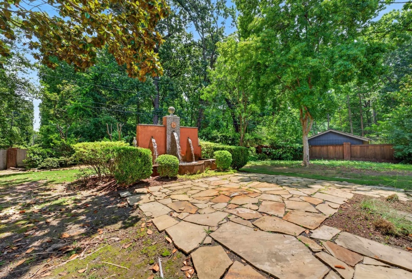 Flagstone patio with a multi-tiered water feature, surrounded by mature trees and manicured shrubbery