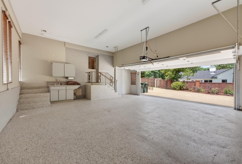 Spacious garage featuring a durable speckled epoxy floor, built-in cabinetry with sink, and a large overhead door
