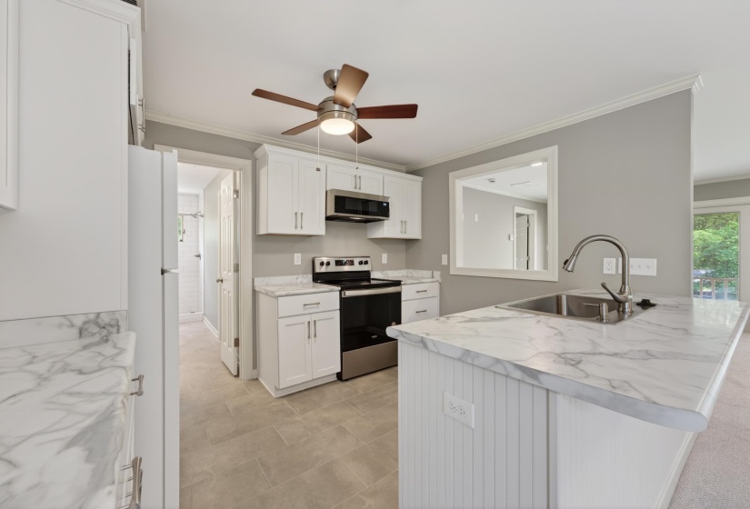 Kitchen featuring white shaker cabinetry, stainless steel appliances, marbled countertops, a peninsula with an integrated sink, and ceiling fan with lighting