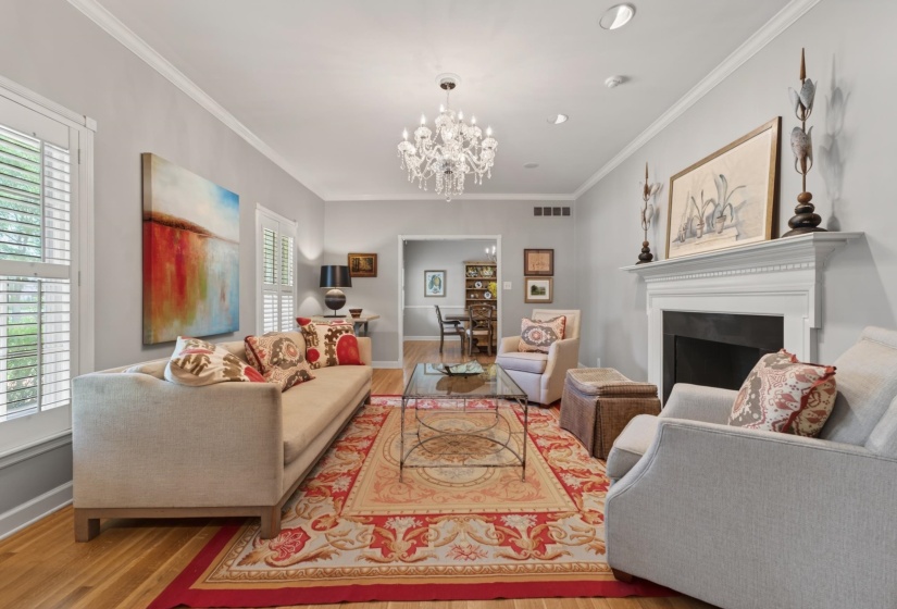 Living room featuring wood-finish flooring, a white mantel fireplace, and a crystal chandelier
