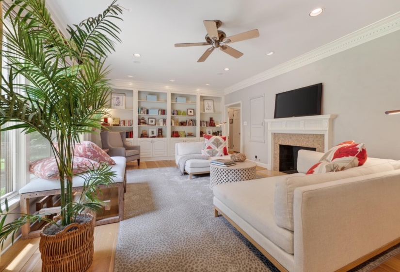 Living area featuring a fireplace with a stone surround and a white mantel, hardwood flooring, built-in shelving, crown molding, and recessed lighting