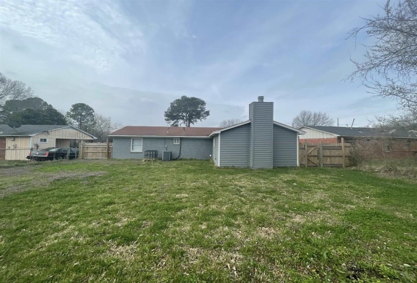 Expansive green space featuring a wood fence, a single-story residence with a gray exterior, and a prominent chimney