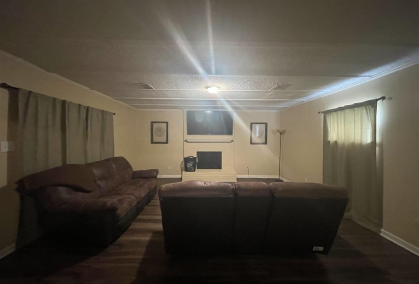 Living area featuring wood-finish flooring, a white brick fireplace with a mantel, and crown molding