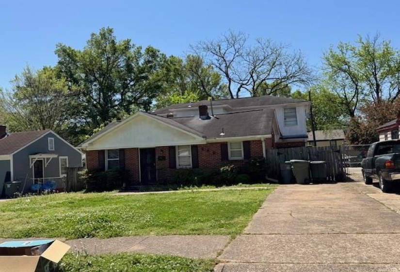 View of front facade featuring driveway, fence, a front lawn, and brick siding