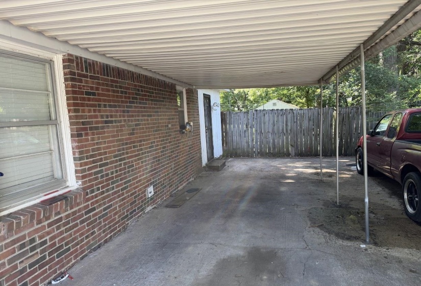Covered carport with a corrugated metal roof, supported by metal poles, offering shelter for vehicles