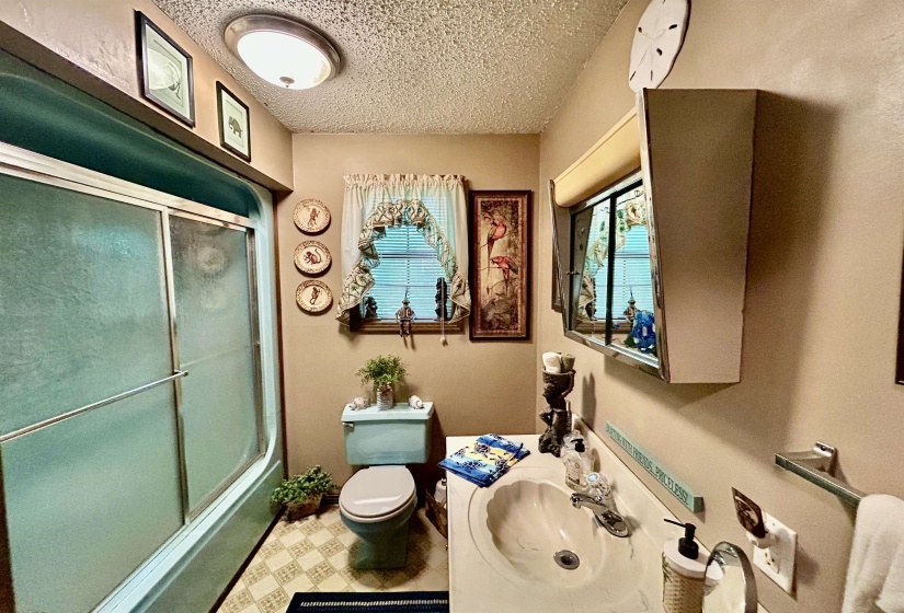 Bathroom featuring a shower with sliding glass doors, a vanity with an integrated sink, a window with blinds, a wall-mounted medicine cabinet, and patterned flooring