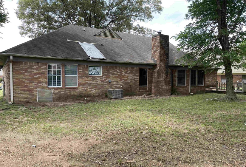 Brick exterior with a prominent brick chimney, multiple windows, a rear entry, and mature trees in the yard