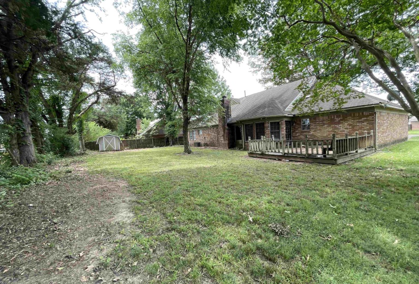 Expansive backyard featuring mature trees, a wooden deck, and a storage shed