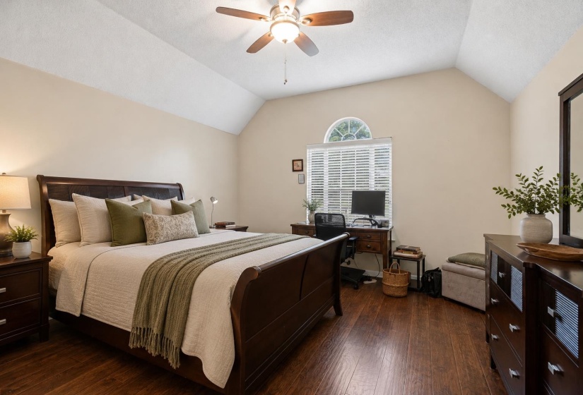 Vaulted ceiling featuring a ceiling fan, wood-finish flooring, and a window with an arched transom