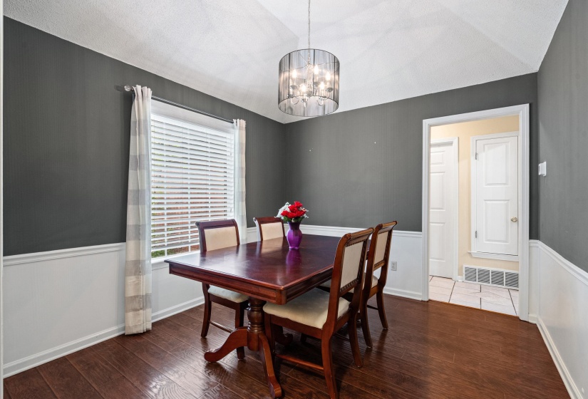 Dining area featuring wood-finish flooring, white wainscoting, and a drum-style pendant light fixture