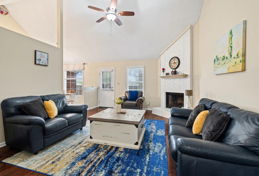 Living area featuring a white-painted brick fireplace, wood mantel, and vaulted ceiling