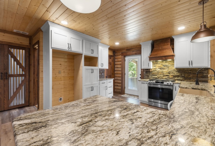 Spacious kitchen featuring an expansive island with a polished countertop, white cabinetry, a built-in stainless steel range, and a wood-paneled ceiling