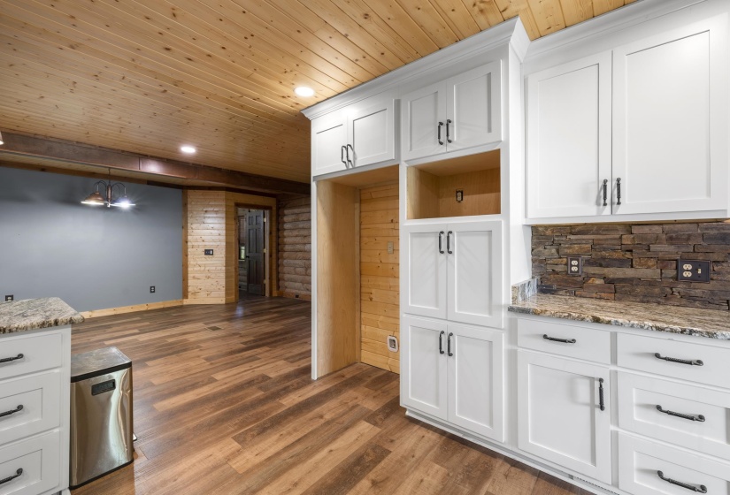 Kitchen space featuring white cabinetry with dark hardware, stone backsplash, and granite countertops