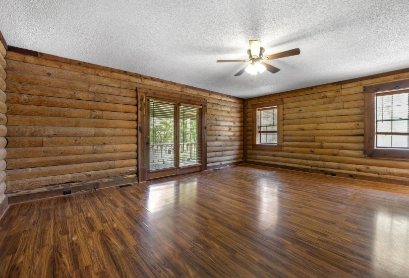 Spacious bedroom room featuring log-style wood paneling, wood-finish flooring, a ceiling fan, dual windows, and sliding glass doors with direct outdoor access