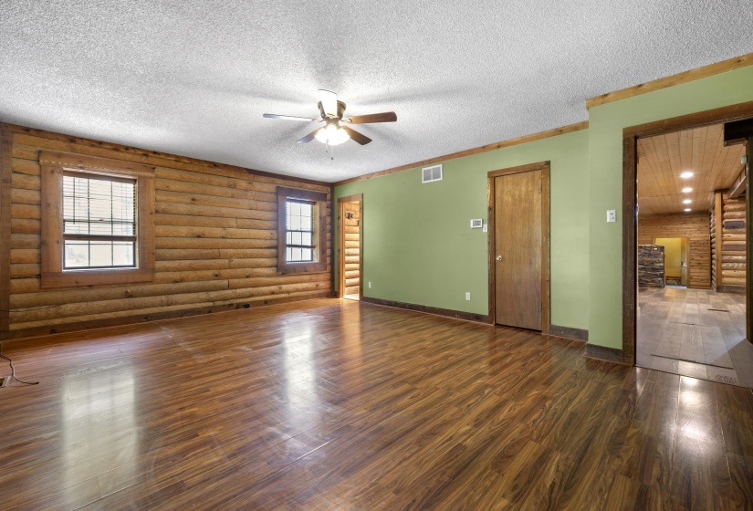 Spacious interior featuring wood-finish flooring, a ceiling fan, and prominent log wall construction