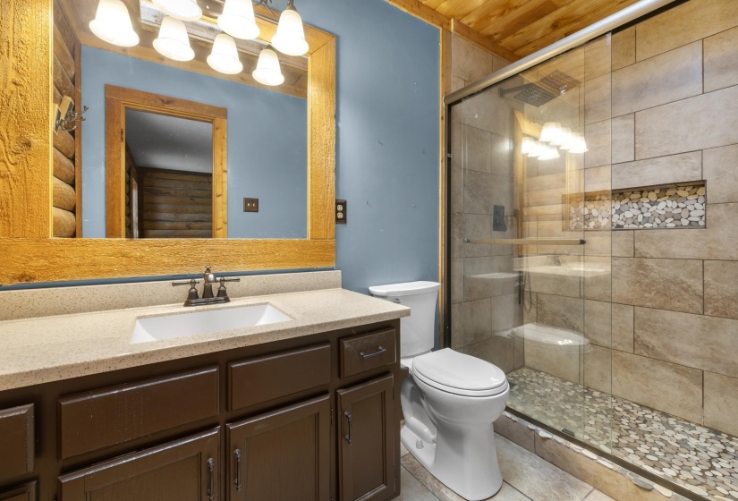 Bathroom featuring a spacious walk-in shower with stone tile surround, decorative pebble inlay, and a pebble floor
