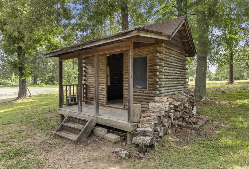 Rustic log cabin structure featuring a small covered porch and wood-stacked exterior