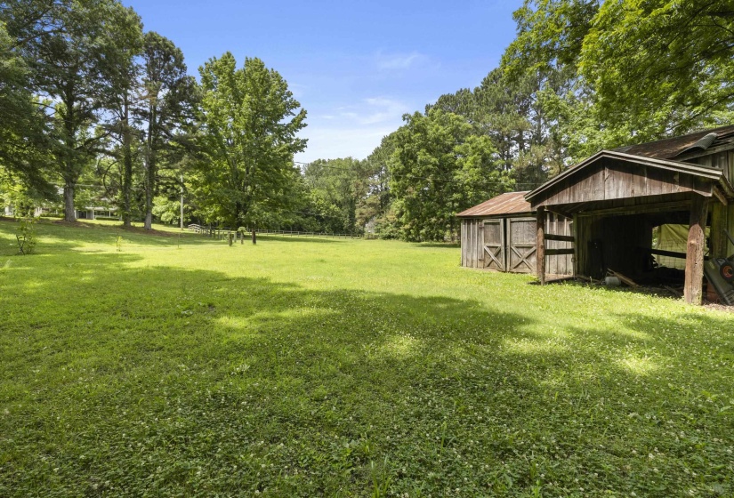 Expansive green space featuring two weathered outbuildings with wood siding and a significant tree canopy