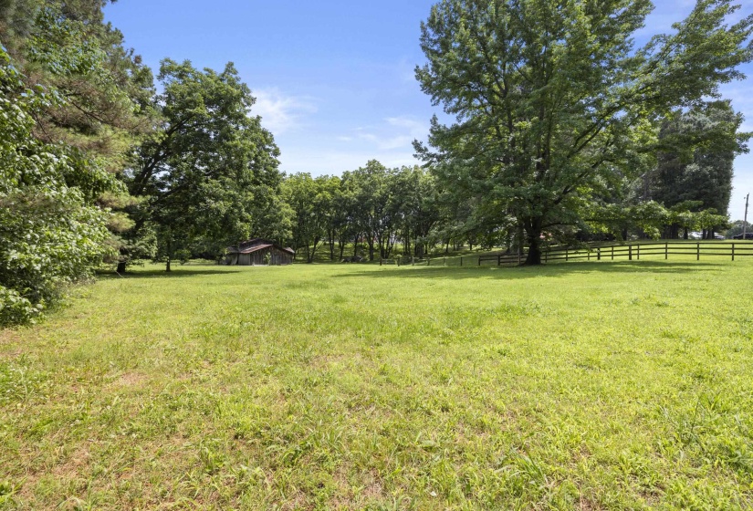 Expansive green field featuring mature trees and a wooden fence bordering the property