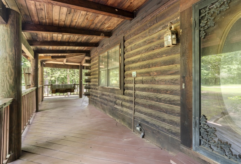 Expansive wood-finish porch featuring a log cabin style exterior, wood ceiling, wood-plank flooring, and a decorative glass door with wrought iron detailing