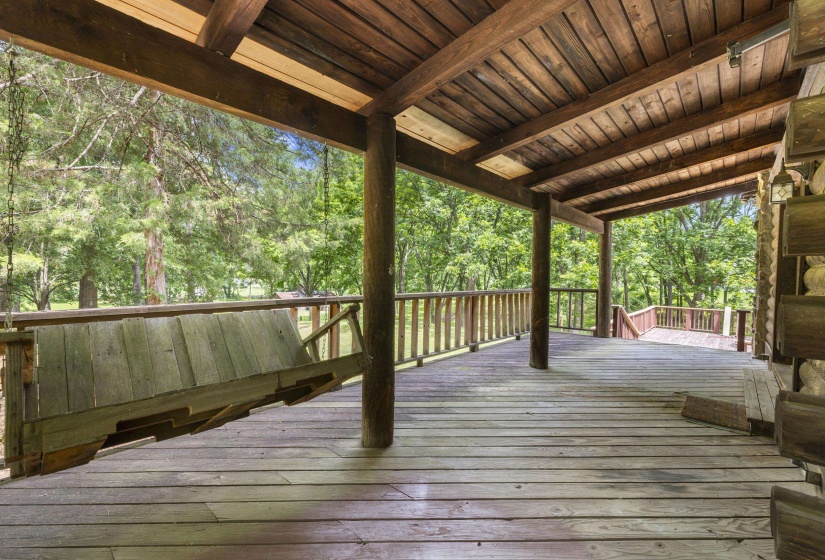 Expansive covered porch featuring a wood plank ceiling and flooring, wood railing, and a rustic wood porch swing