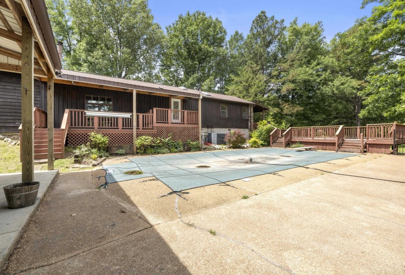 Outdoor swimming pool with a protective cover, surrounded by a concrete patio and a multi-level wood deck