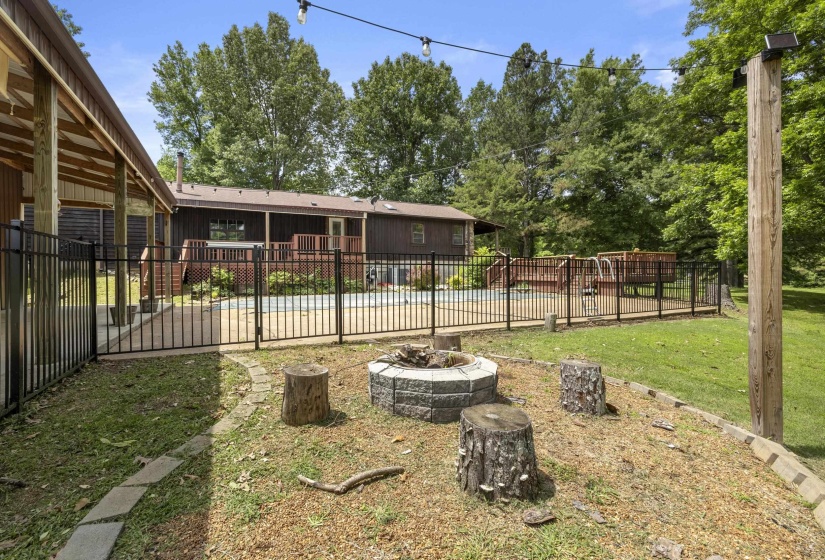 Outdoor living area featuring a stone-clad fire pit, mature trees, and string lighting